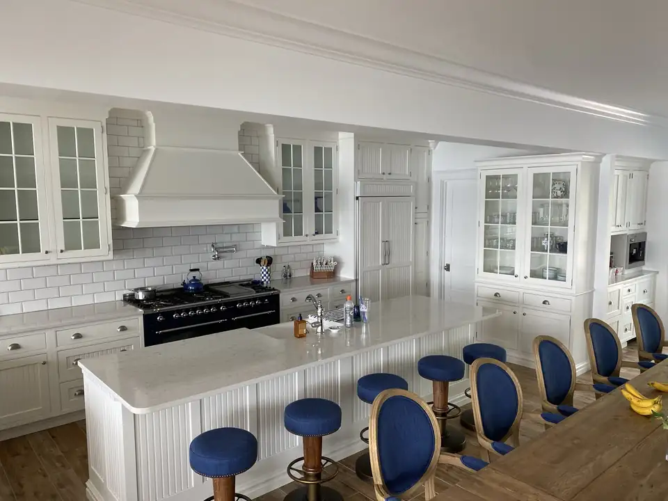 Bright white kitchen with a long island, blue bar stools, range hood and glass-front cabinets, kitchen design Cochranton