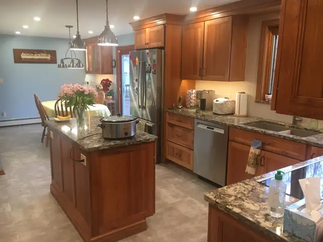 Cherry kitchen with a granite island, stainless dishwasher and pendant lights