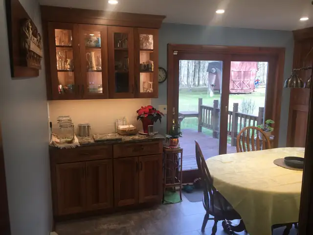 Glass-front cherry hutch cabinets with lighting beside a dining table and deck doors