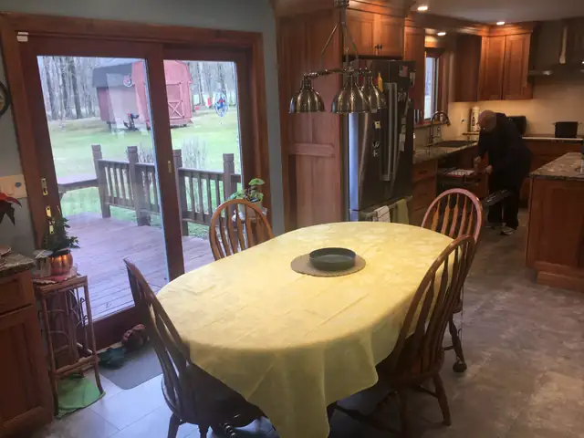 Dining table beside a cherry kitchen with granite counters and a glass door to the deck