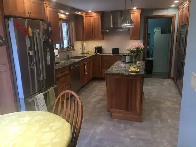 View across a finished cherry kitchen with island, stainless refrigerator and tile floor