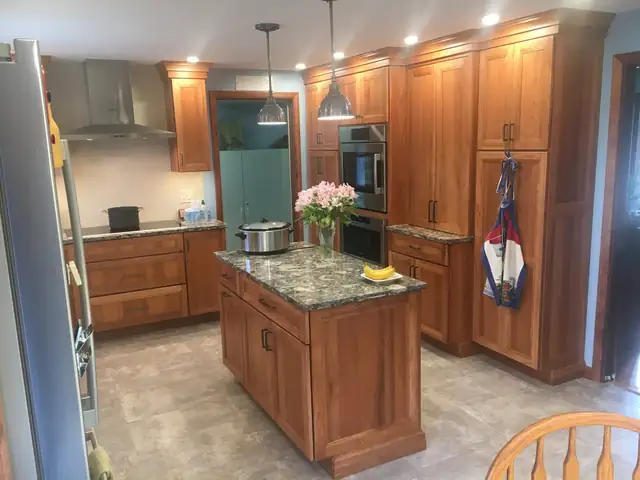 Cherry wood kitchen with a granite-topped island, pendant lights and tall pantry cabinets