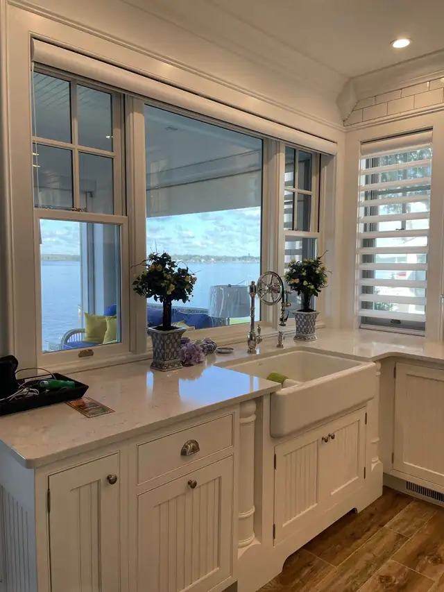 White farmhouse sink under a window with a water view, potted plants on the counter
