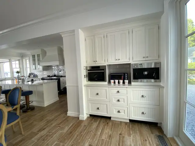 Wall of white painted cabinets with built-in microwave, oven and drawers beside a dining area